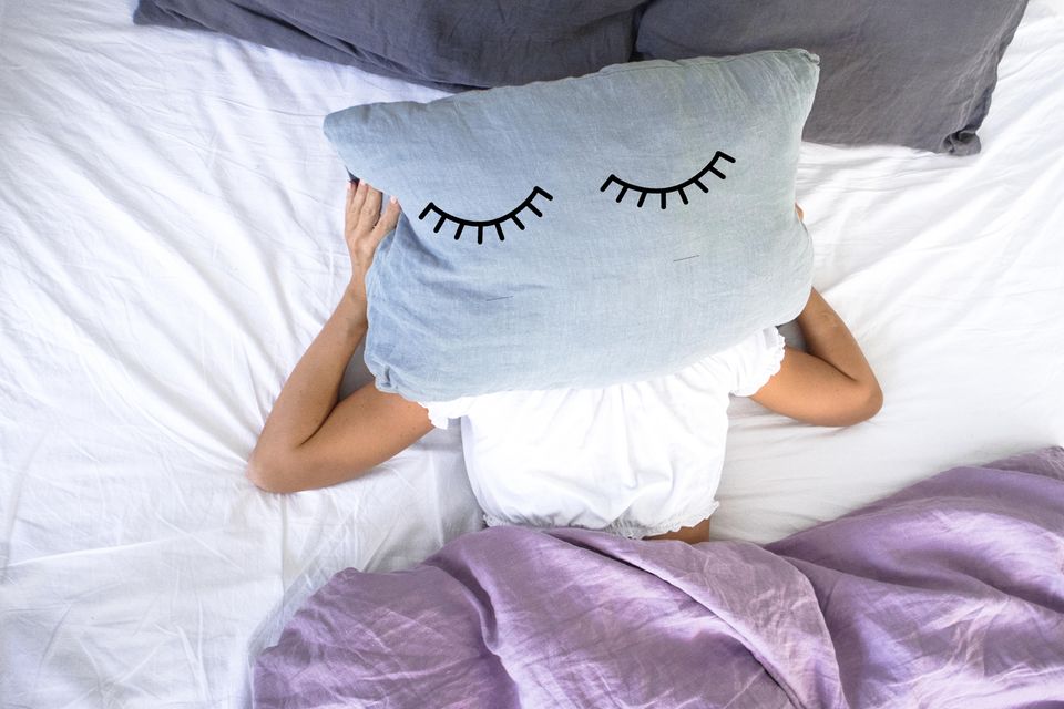 Augenschatten: Frau liegt im Bett und hält Kissen über dem Kopf