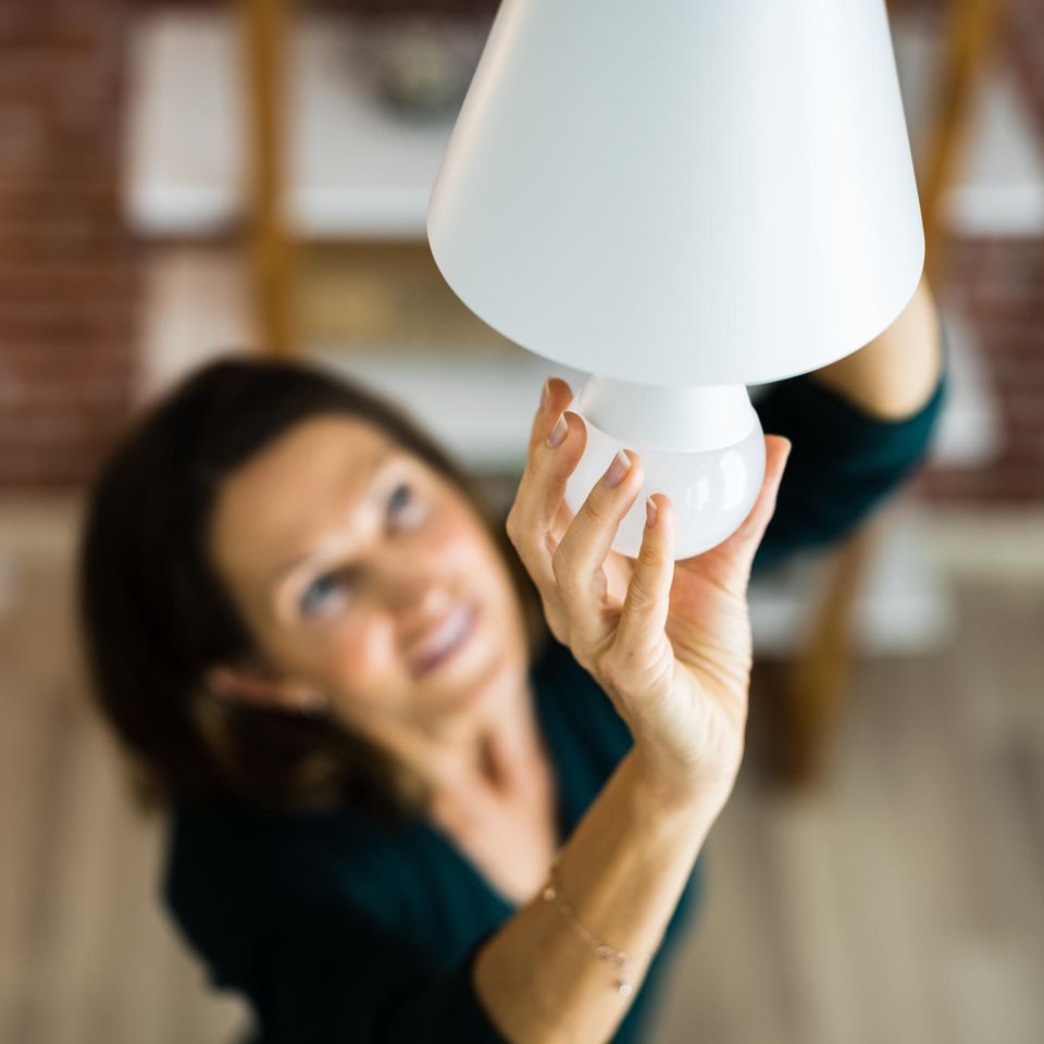 Eine Frau dreht eine neue Glühbirne in eine Lampe ein