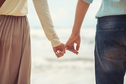 Dieses Wort gefährdet Beziehungen: Mann und Frau halten mit den kleinen Fingern Händchen am Strand