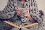 Tipps bei Kälte: Frau auf der Couch mit Decke um die Schultern