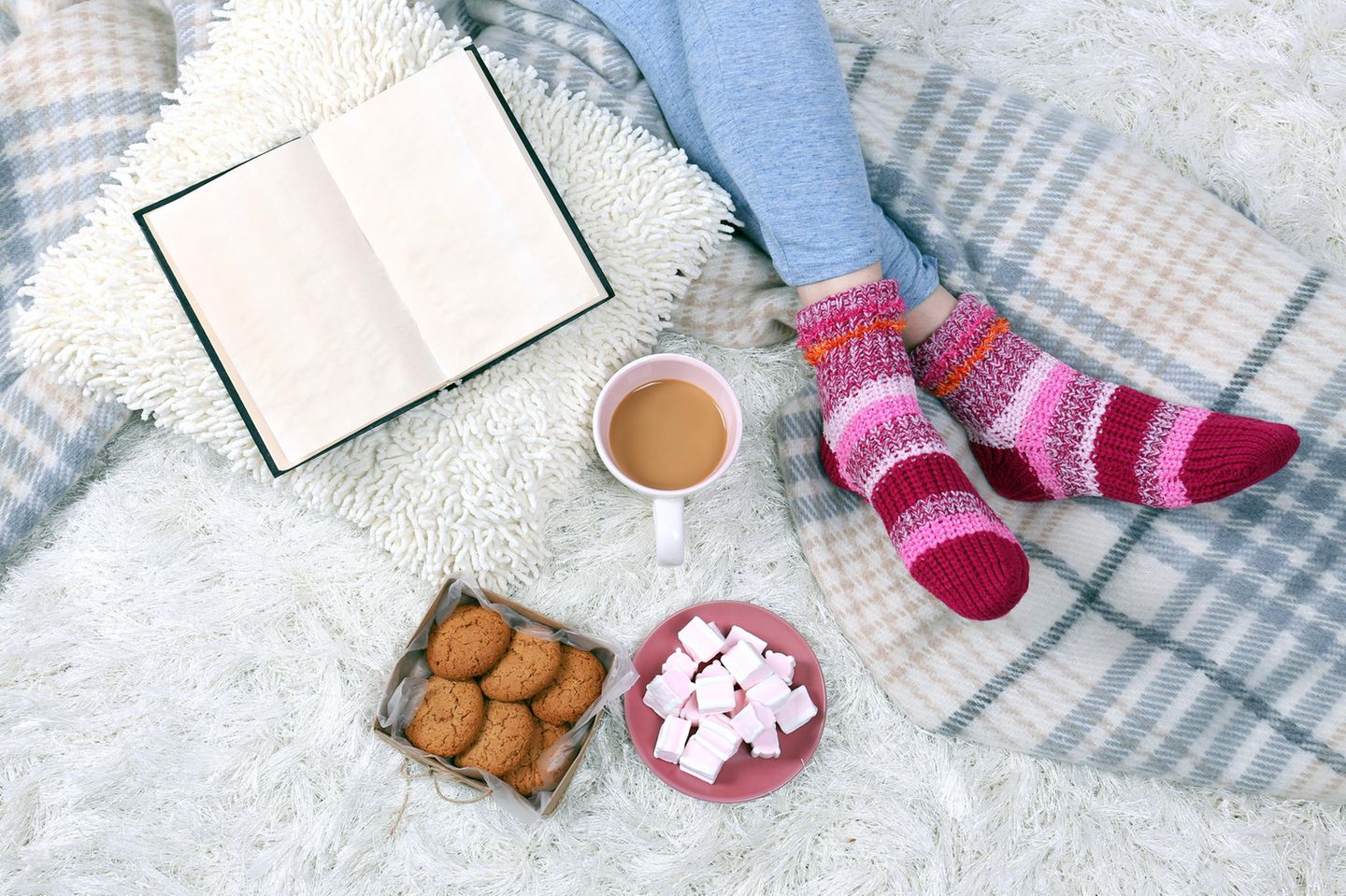 Tipps bei Kälte: Frau sitzt mit selbstgestrickten Socken an den Füßen auf dem Bett
