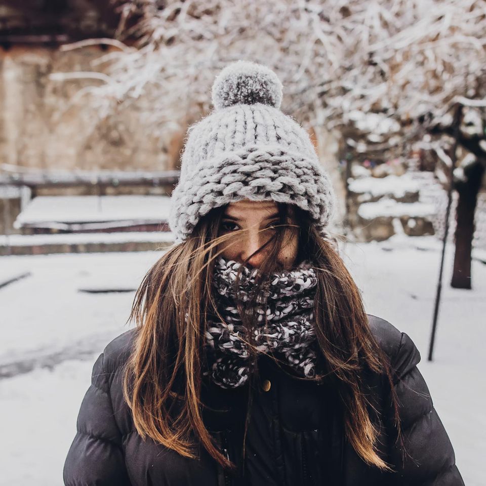 Tipps bei Kälte: Eine dick eingepackte Frau mit Mütze im Schnee