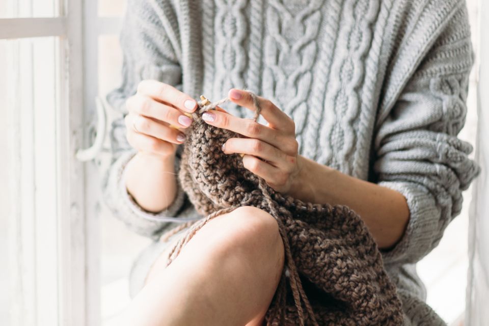 Selber stricken: Die besten Pullover: Frau im Strickpulli sitzt auf einem Stuhl und strickt