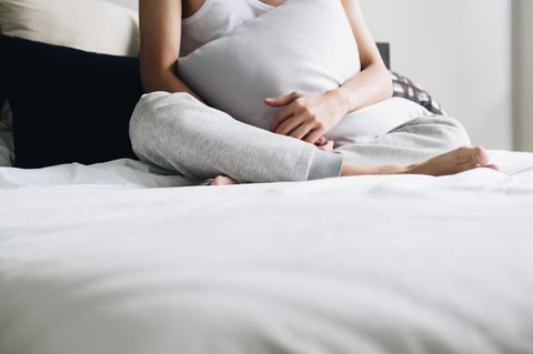 MiSELF-Studie: Frau sitzt mit Kissen vor dem Bauch auf dem Bett