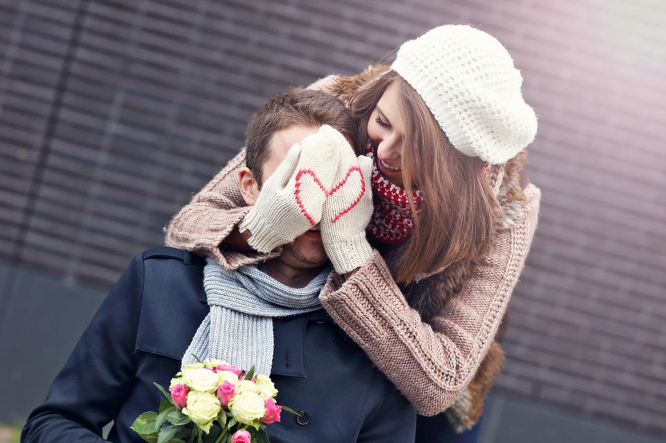 Liebeserklärung: Frau mit Herzchen-Handschuhen hält Mann von hinten die Augen zu