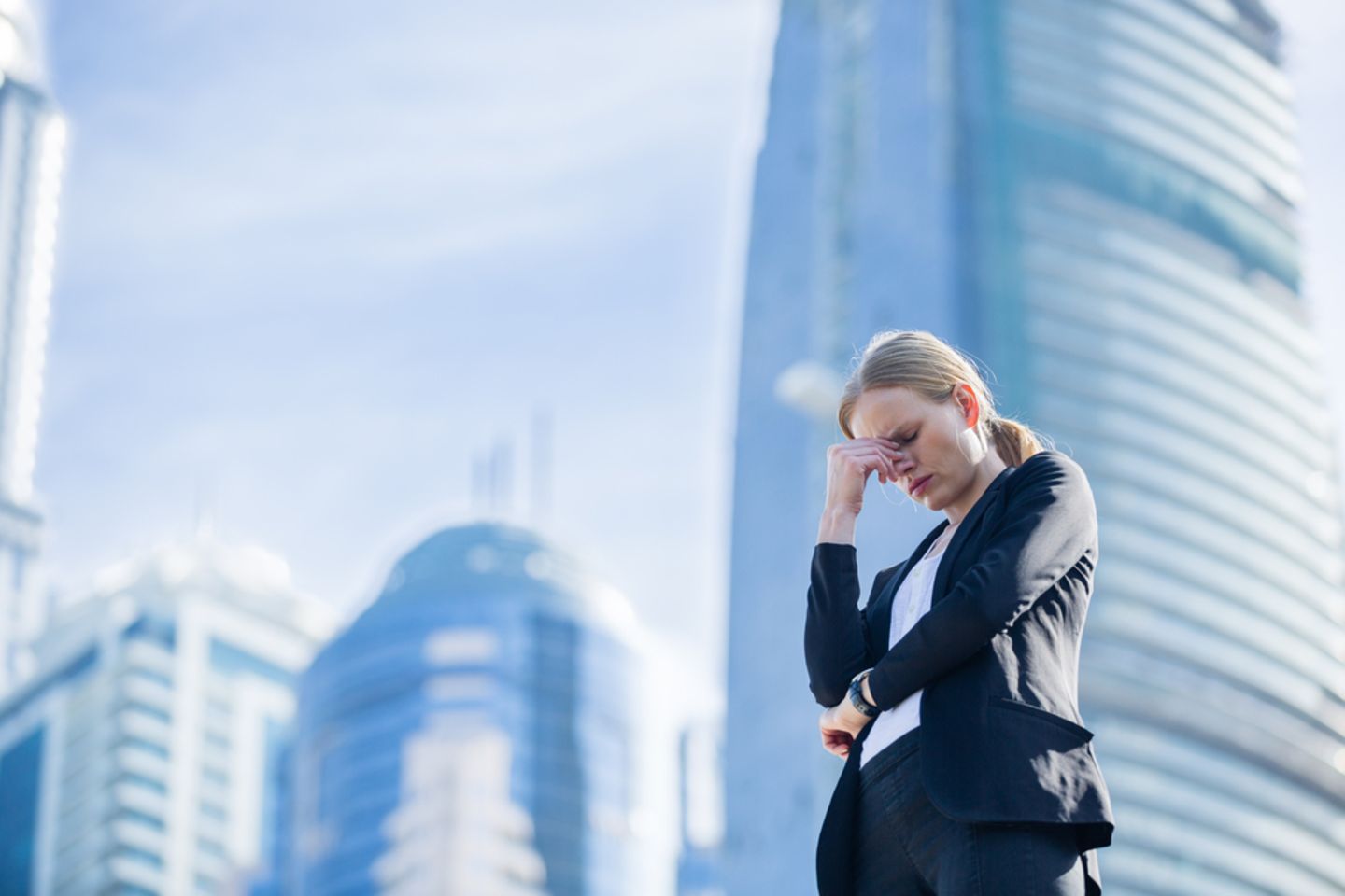 Angst vor der Arbeit – das solltest du tun: Gestresste Frau steht vor Bürogebäuden und fasst sich an den Kopf
