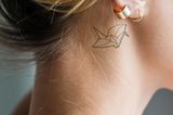 Tattoo Motive: Eine Frau mit einem zarten Origami-Schwan hinterm Ohr
