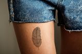 Tattoo Motive: Eine Frau mit einem Feder-Tattoo auf dem Oberschenkel