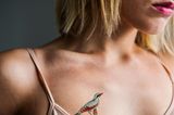 Tattoo Motive: Eine Frau mit einem kleinen Specht-Tattoo über der rechten Brust