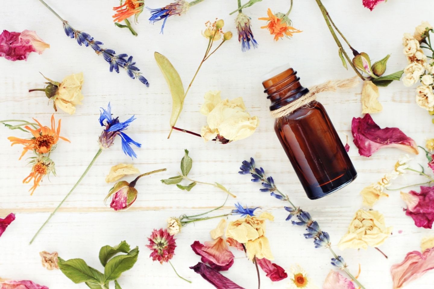 Massageöl selber machen: schnell und unkompliziert: Viele getrocknete Blüten und eine kleine dunkle Flasche