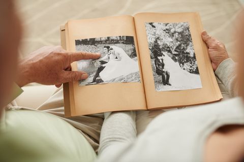 Gnadenhochzeit: Bedeutung, Geschenke und Glückwünsche: Älteres Pärchen blättert in einem alten Fotoalbum mit Hochzeitsbildern