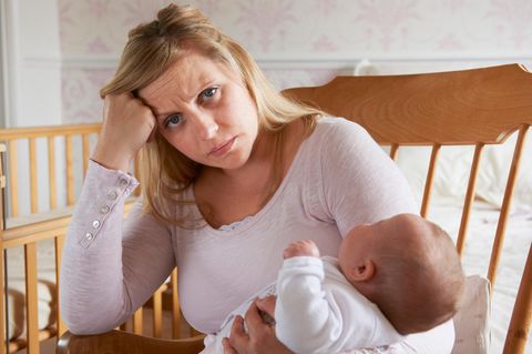 Selbstliebe: Mutter sitzt fertig im Schaukelstuhl mit Baby