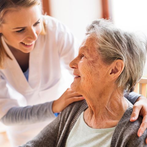 Altenpfleger Gehalt: Altenpflegerin legt Hände auf Schulter einer älteren Frau