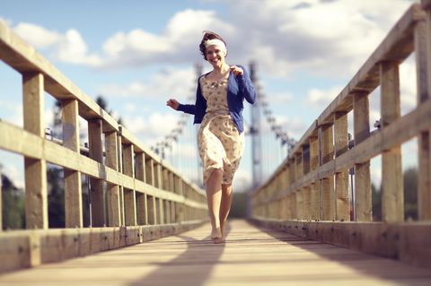 Mit diesem Glücks-Trick gehst du fröhlicher durchs Leben: Eine Frau geht tänzelnd über eine Brücke