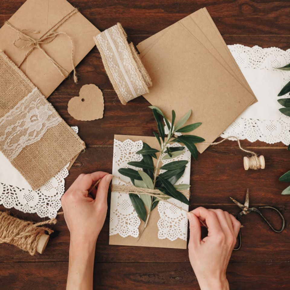 Hochzeitseinladungen selber machen - die schönsten Ideen: Frau bindet Zweig mit Sisalbändchen um eine Karte