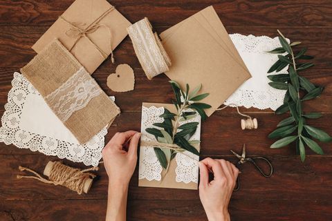 Hochzeitseinladungen selber machen - die schönsten Ideen: Frau bindet Zweig mit Sisalbändchen um eine Karte