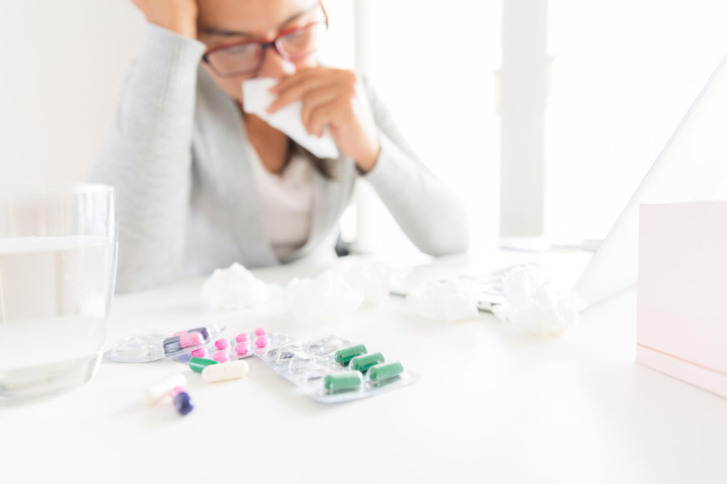 Krank in der Probezeit: Das solltest du wissen: Frau sitzt mit Taschentüchern und Medikamenten am Schreibtisch