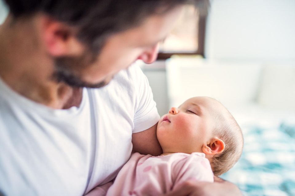 Elternzeit als Vater: Mann hält Baby im Arm