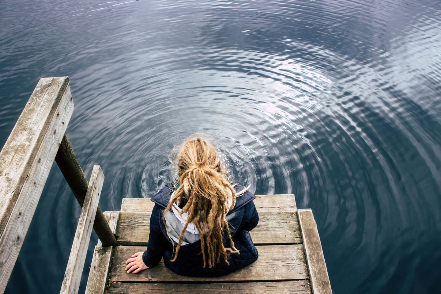 Selbstzweifel: Eine junge Frau sitzt grübelnd am See