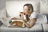 Gewohnheiten erfolgreicher Frauen: Eine Frau liegt auf dem Sofa und isst Pizza