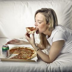 Gewohnheiten erfolgreicher Frauen: Eine Frau liegt auf dem Sofa und isst Pizza