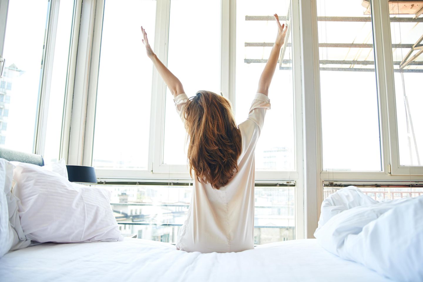 Gewohnheiten erfolgreicher Frauen: Eine Frau sitzt auf dem Bett und streckt sich