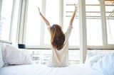 Gewohnheiten erfolgreicher Frauen: Eine Frau sitzt auf dem Bett und streckt sich