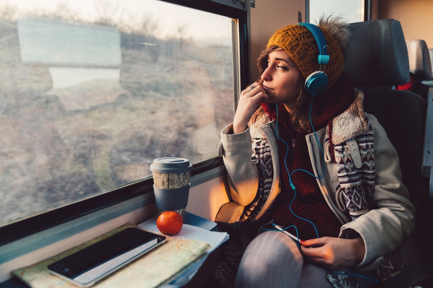 Frau sitzt in Bahn, hört Musik und schaut aus dem Fenster