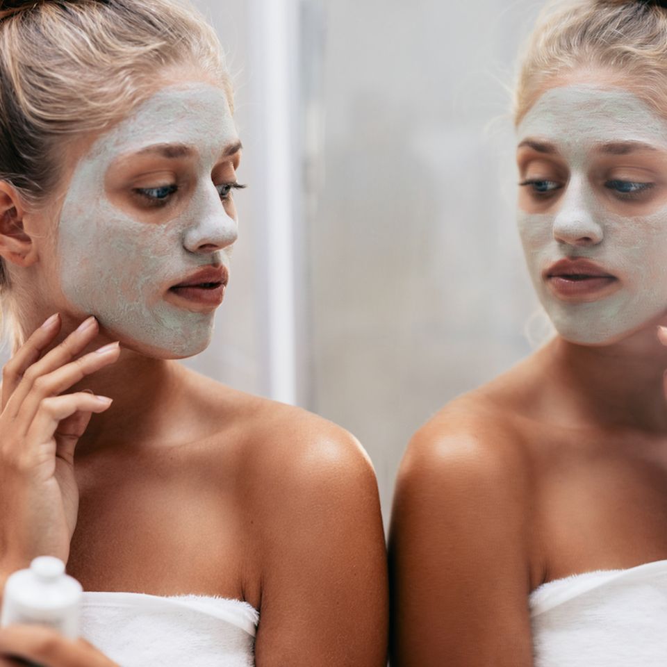 Hautprobleme durch Stress: Frau schaut sich ihr Gesicht im Spiegel an