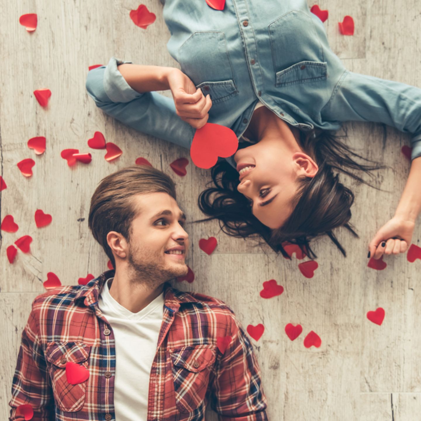 Eheversprechen: praktische Tipps und Beispiele: Pärchen liegt auf dem Boden und sieht sich an, um sie herum rote Papierherzen