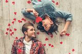 Eheversprechen: praktische Tipps und Beispiele: Pärchen liegt auf dem Boden und sieht sich an, um sie herum rote Papierherzen