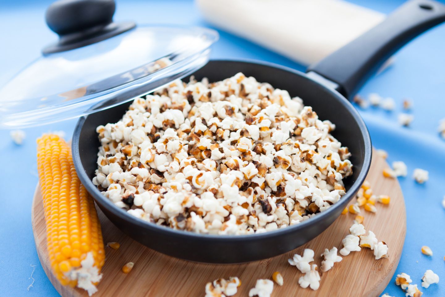 Popcorn selber machen: So leicht geht das Rezept: Pfanne gefüllt mit Popcorn steht auf einem Brett, ein Maiskolben liegt daneben