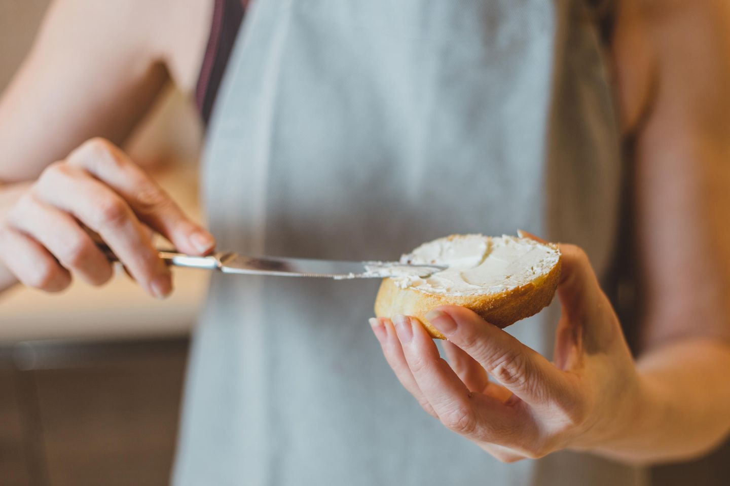 Frischkäse in der Schwangerschaft: Frau streicht Frischkäse auf ein Brot