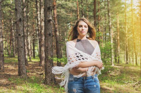 Stola häkeln: Anleitung und Ideen: Frau steht im Wald, ein Dreieckstuch um die Schultern gewickelt