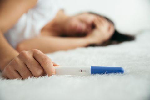 Unerfüllter Kinderwunsch: Frau liegt mit negativem Schwangerschaftstest auf weißem Teppich