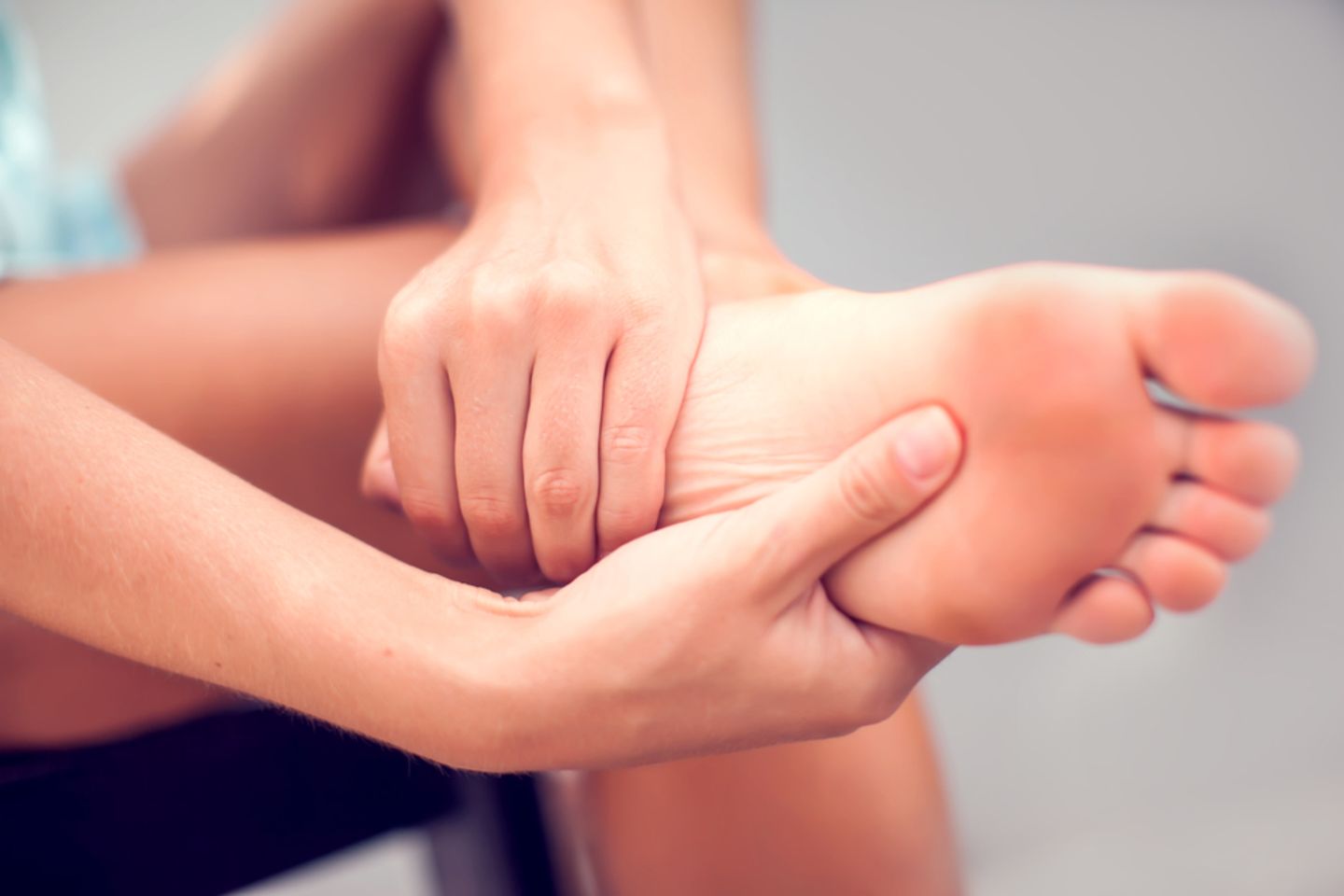 Fersensporn: Ursache und Behandlung: Frau umfasst Ferse und Fußsohle mit den Händen vor Schmerzen