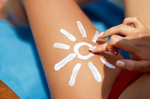 Sunblocker: Frau trägt Sonnencreme auf Oberschenkel in Form einer Sonne auf