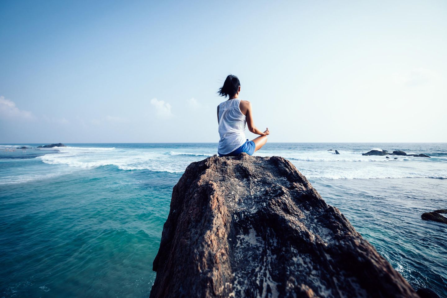 Mentales Training: Frau meditiert auf Felsen am Meer