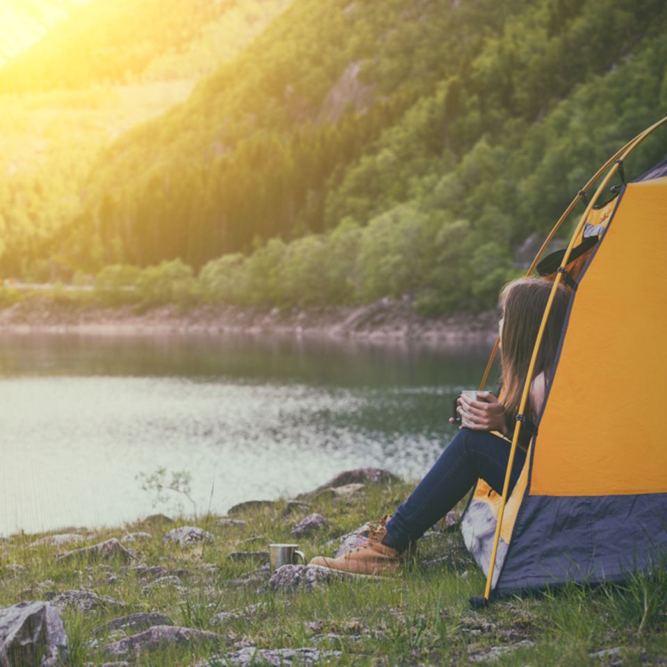 Packliste Camping: Checkliste zum Ausdrucken: Frau sitzt im Zelt und guckt heraus in die Landschaft