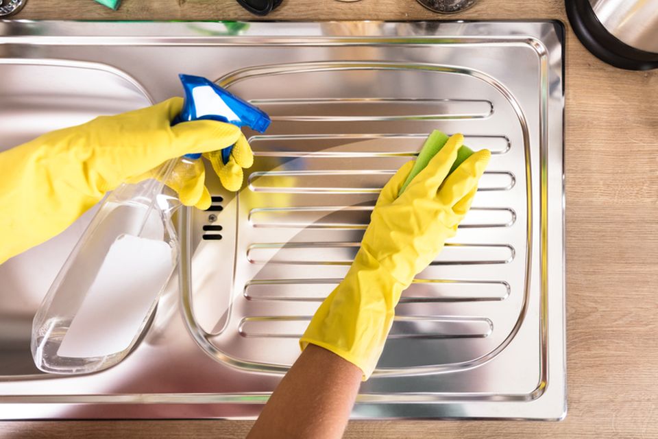Edelstahl reinigen: 4 effektive Hausmittel. Spüle wird besprüht und sauber gewischt