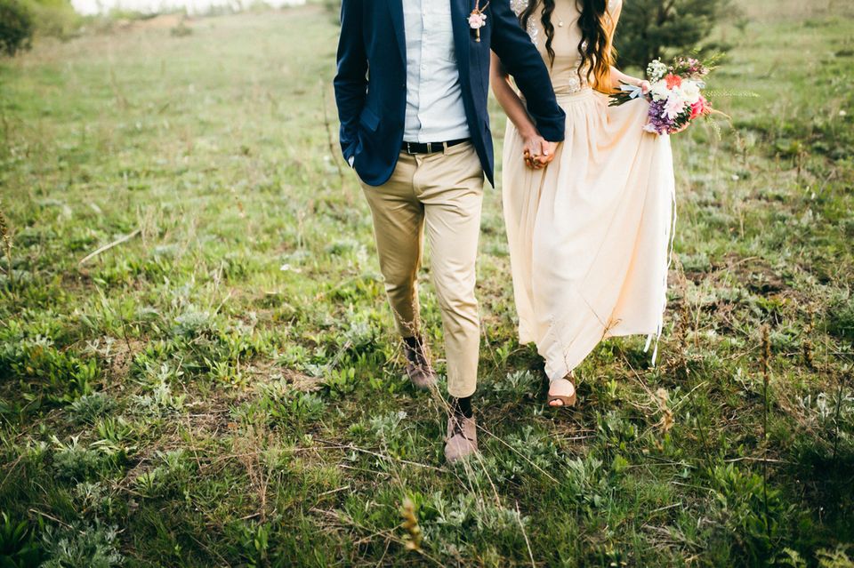 Brautpaar läuft Händchen haltend über Wiese