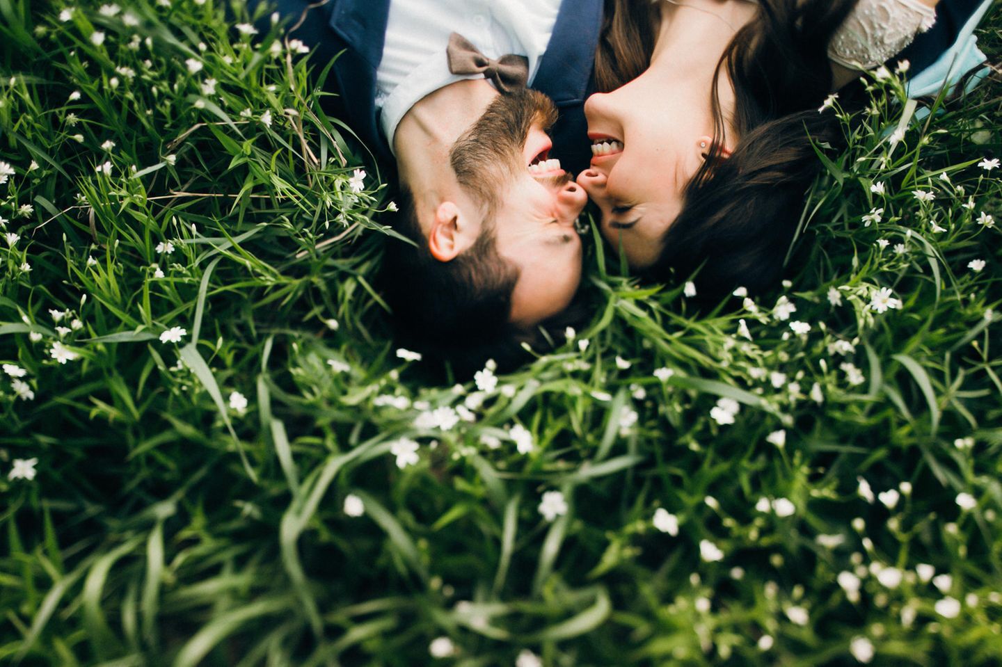 Petersilienhochzeit: Bräuche, Deko und Outfit-Ideen: Brautpaar liegt im Grünen Gesicht an Gesicht und freut sich