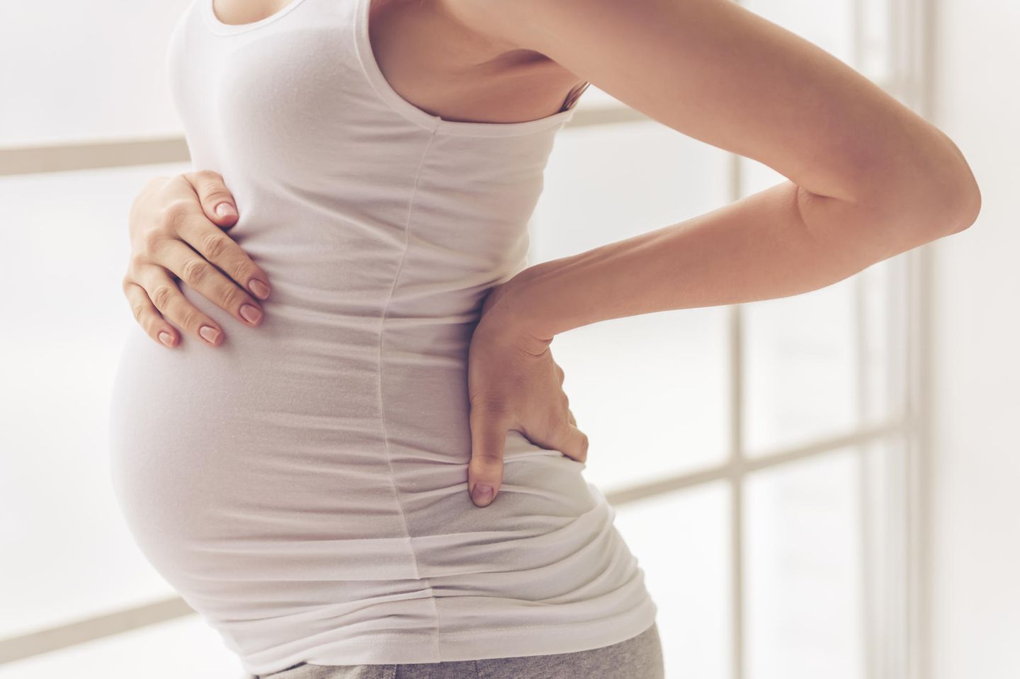 Rückenschmerzen Schwangerschaft: Schwangere stützt Hand in Rücken