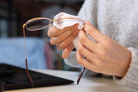 Brille putzen: Frau putzt Brille mit Mikrofasertuch