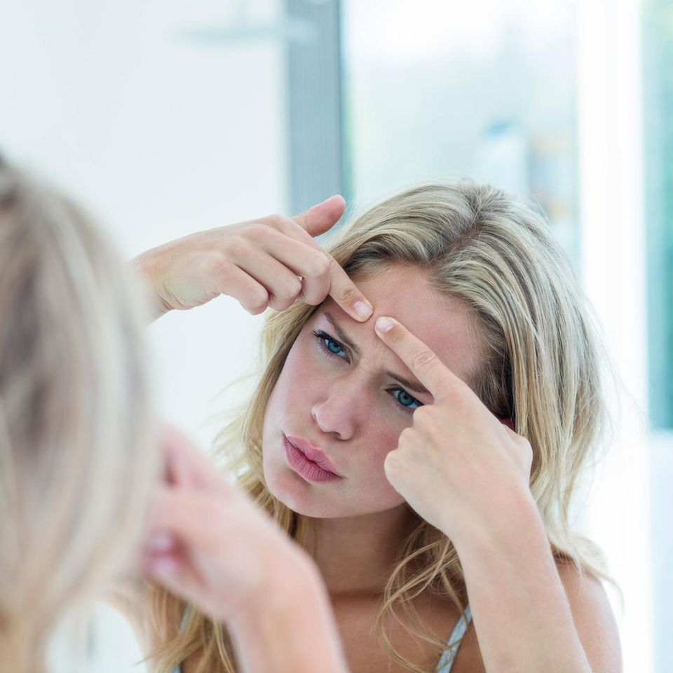Unterirdische Pickel: Frau steht vor dem Spiegel und drückt Pickel auf der Stirn aus