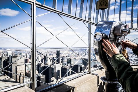 Die teuersten Touristenattraktionen weltweit: Frau steht an Teleskop und blickt über Manhattan, New York City