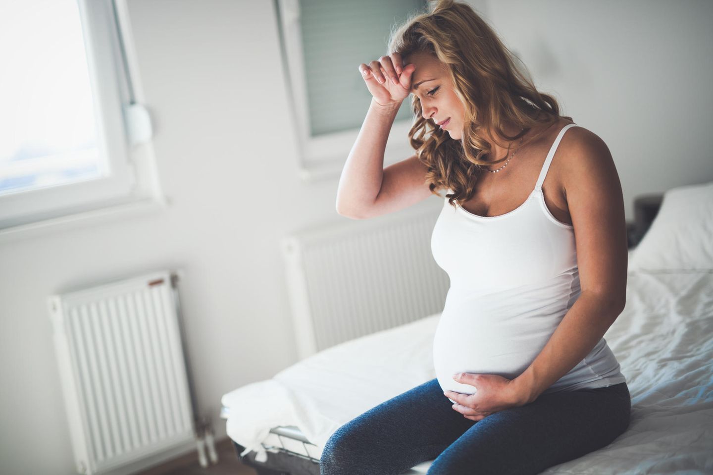 Kopfschmerzen in der Schwangerschaft: Schwangere sitzt auf Bett und hält sich die Hand an den Kopf