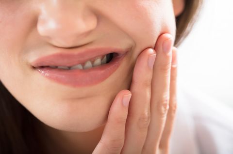 Entzündung im Mund: Frau fast sich an die Wange mit verzerrtem Gesicht