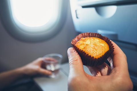 Darf man Essen mit ins Flugzeug nehmen? Was erlaubt ist: Mensch mit Muffin in der Hand sitzt im Flugzeug