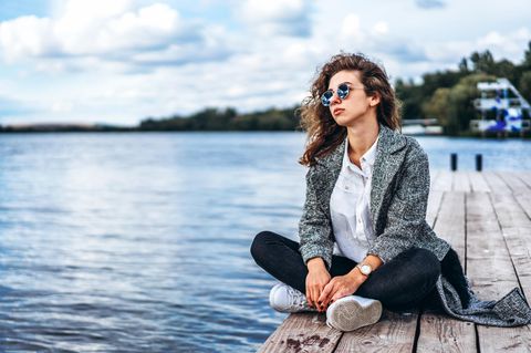 ElitePartner-Studie: Eine nachdenkliche Frau sitzt auf einem Steg am See